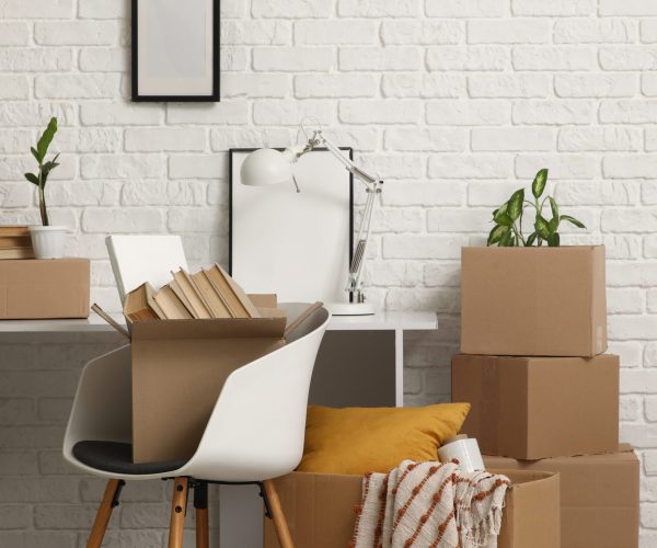Workplace with cardboard boxes near white brick wall in room on moving day