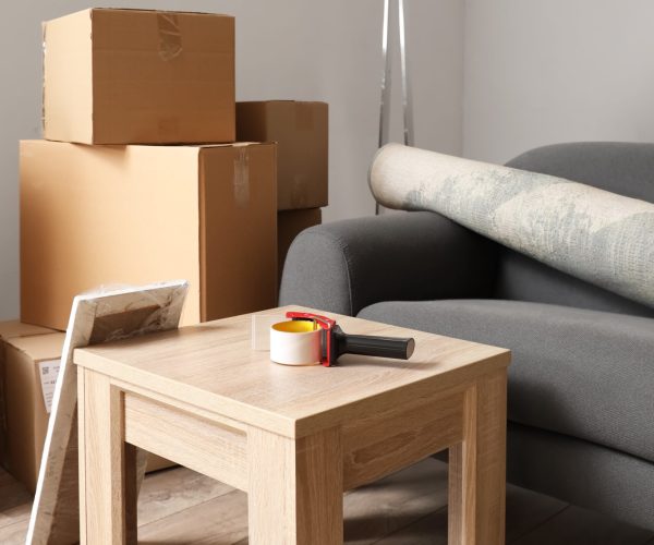 Cardboard boxes with black sofa, rolled carpet and table in living room on moving day