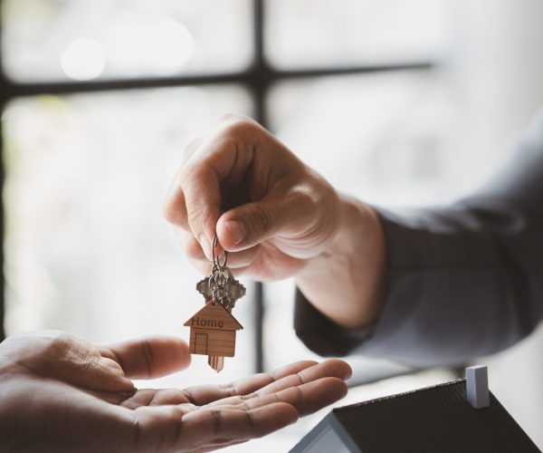 A home rental company employee is handing the house keys to a customer who has agreed to sign a rental contract, explaining the details and terms of the rental. Home and real estate rental ideas.